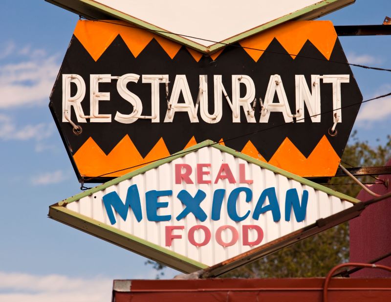 A colorful plate of delicious Mexican food with a hole-in-the-wall restaurant sign in the background.