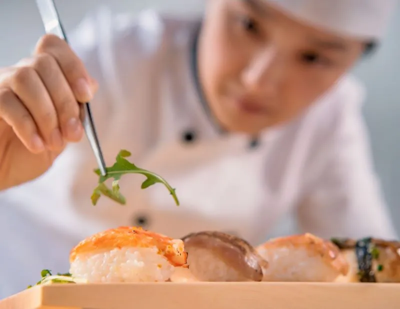 A chef demonstrates the art of sushi rolling to a group of students.