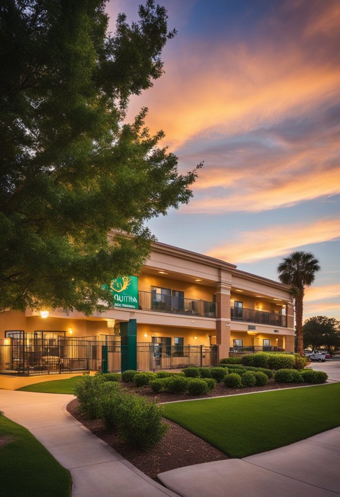 The sun sets behind La Quinta Inn & Suites by Wyndham Waco Baylor Downtown, casting a warm glow on the modern facade and lush landscaping