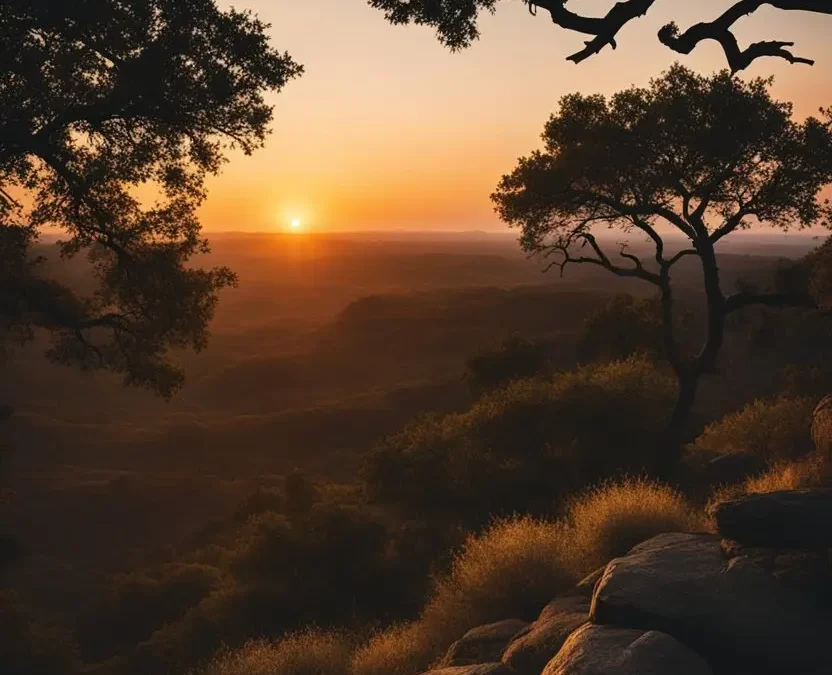 Sunset Hike in Waco Texas - The sun sets behind the rolling hills of Waco, casting a warm orange glow over the rugged landscape. Silhouetted trees and rocky outcrops dot the horizon.