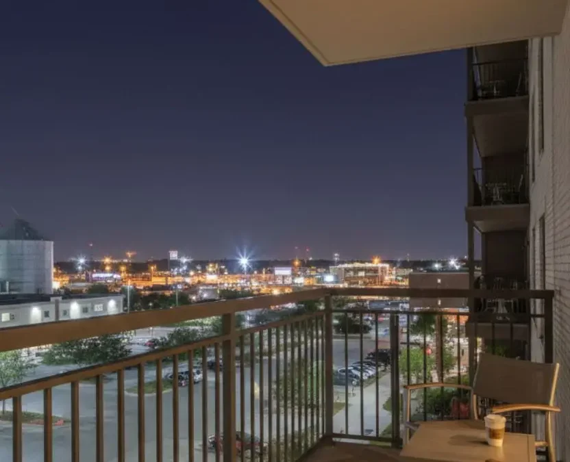 A view from a midscale hotel balcony at night in Waco, Texas, featuring outdoor seating and a view of the city skyline and silos.