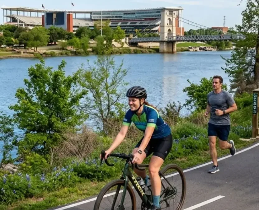 Cyclists and runners enjoying the scenic paved Hike and Bike Trails in Waco Texas alongside the river with downtown landmarks in the background.